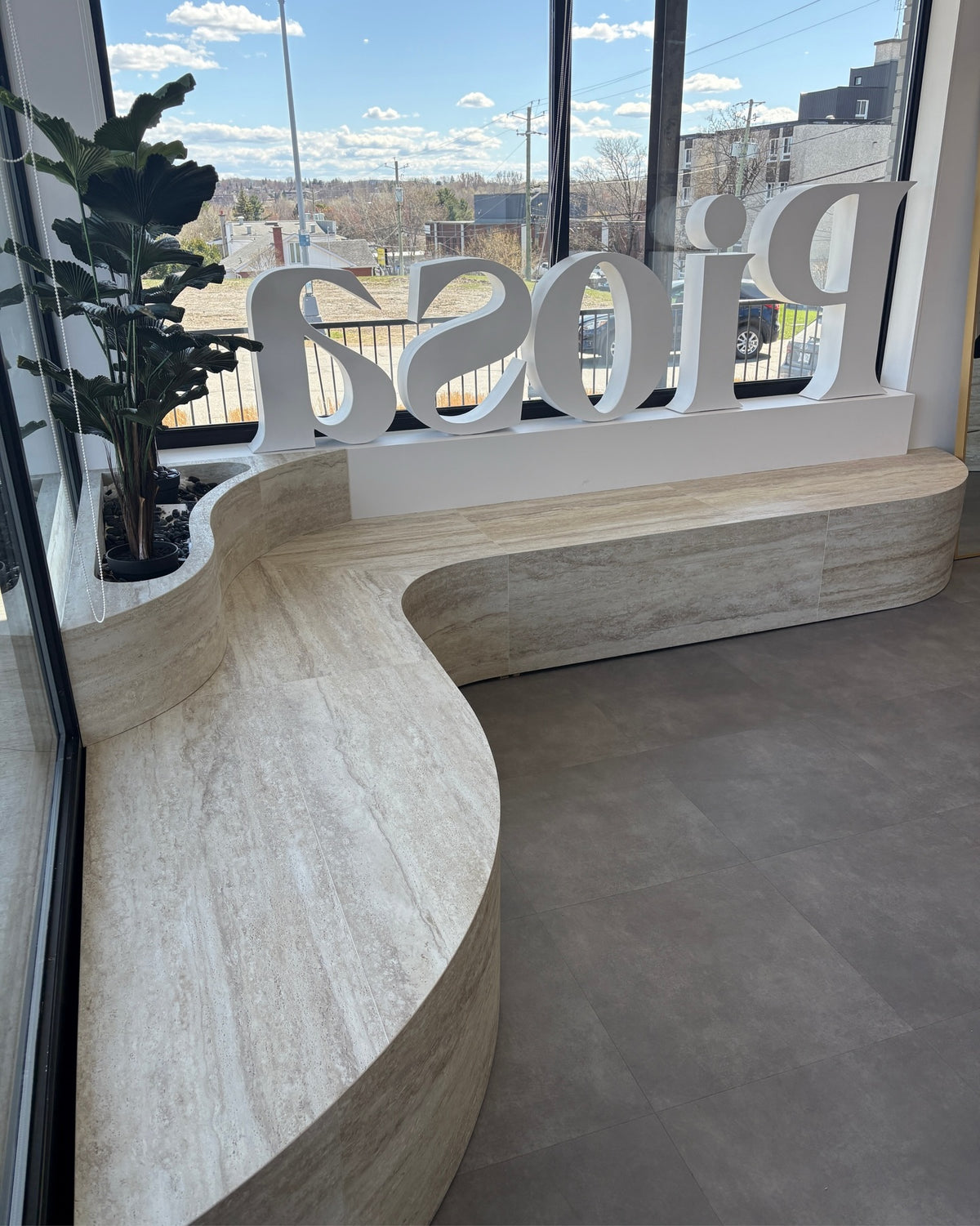 Banc courbe habillé du panneau flexible BétonFlex effet travertin beige devant la vitrine de la boutique Piosa